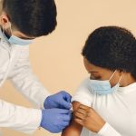 Profissional de saúde aplica uma vacina no braço de uma mulher em um ambiente clínico.