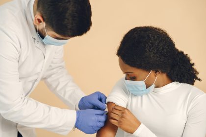 Profissional de saúde aplica uma vacina no braço de uma mulher em um ambiente clínico.